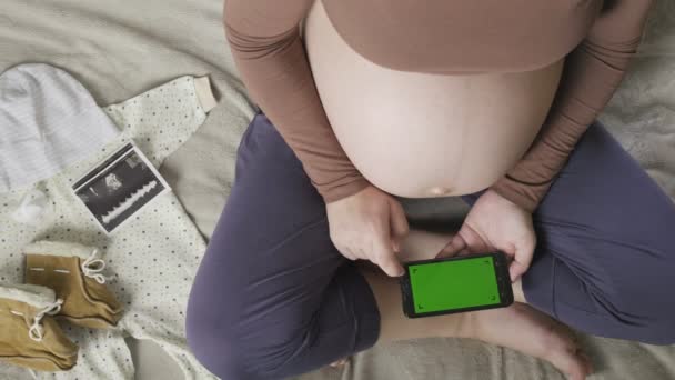 expecting pregnant woman with large belly using smartphone with chromakey on bed - Footage, Video