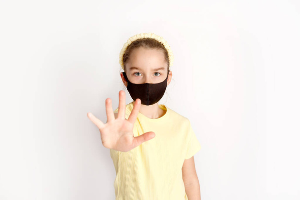 Een schoolmeisje met een zwart beschermend masker vestigt de aandacht op de juistheid en het verplicht dragen van beschermende maskers.  - Foto, afbeelding