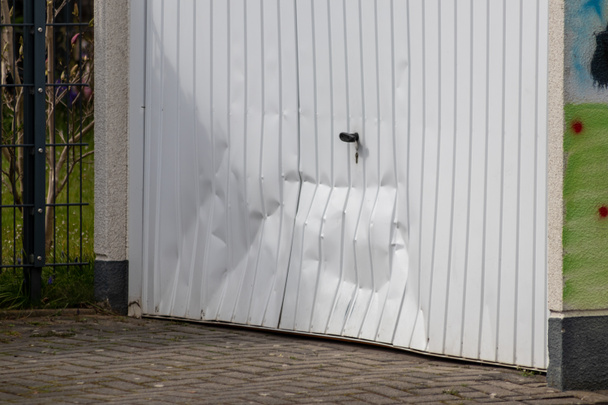Beyaz hasarlı garaj kapısı, sarhoş sürücünün garajı tahrip ettiği kazadan sonraki kazayı gösteriyor. - Fotoğraf, Görsel
