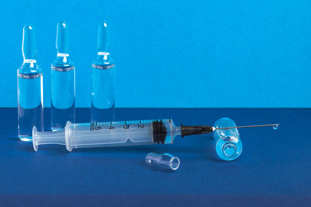 針の上に薬のドロップを持つ注射器は、開いたアンプルに横たわっています。青の背景. - 写真・画像