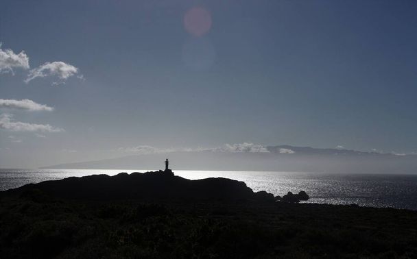Faro de Punta de Teno, construido en 1893 en la isla de Tenerife. La isla de la Gomera con nubes y la brillante superficie del océano Atlántico, en el horizonte. Islas Canarias, España. - Foto, Imagen