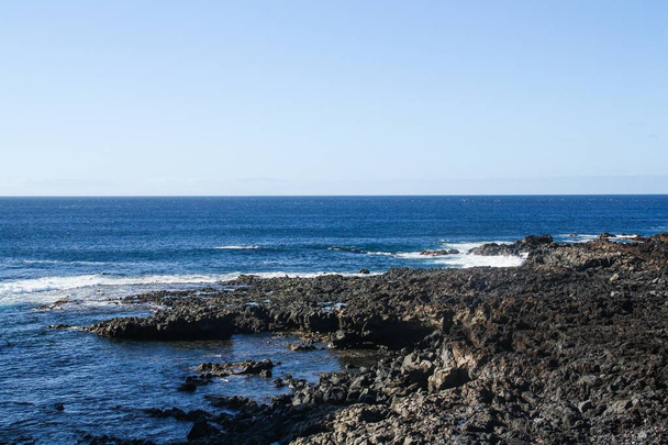 Playa de roca volcánica en el sur de la isla de Tenerife, Islas Canarias, España. Olas golpeando las rocas en un día de mar tranquilo. - Foto, Imagen