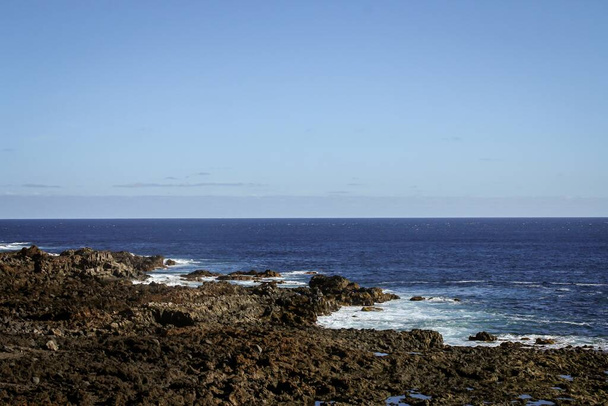 Strand aus Vulkangestein im Süden der Insel Teneriffa, Kanarische Inseln, Spanien. Wellen schlagen an einem ruhigen Tag auf dem Meer auf die Felsen. - Foto, Bild