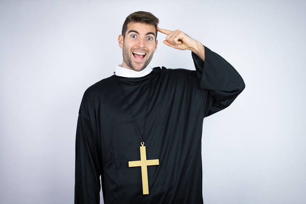 Fiatal spanyol férfi, papi egyenruhát visel, fehér háttér fölött áll, mosolyog, és azt hiszi, hogy van egy ötlete.. - Fotó, kép