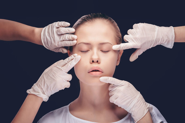 Young woman with eyes closed having an medical exam of her face skin by plastic doctors - Photo, image