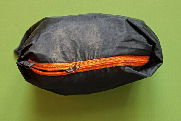 jeden černý plátěný sáček s oranžovým zipem stojí na zeleném stole - Fotografie, Obrázek