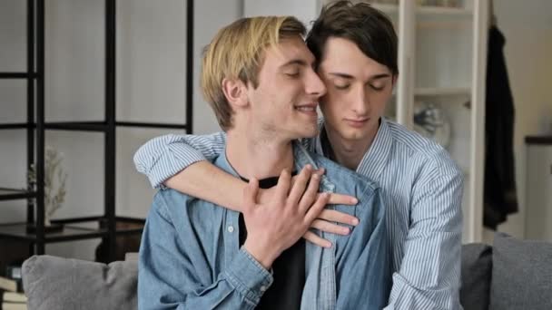 Однополые отношения, непонятная концепция. Любящие гей пара проводит время вместе дома на диване, они обнимают и ласкают друг друга, счастливы быть вместе - Кадры, видео