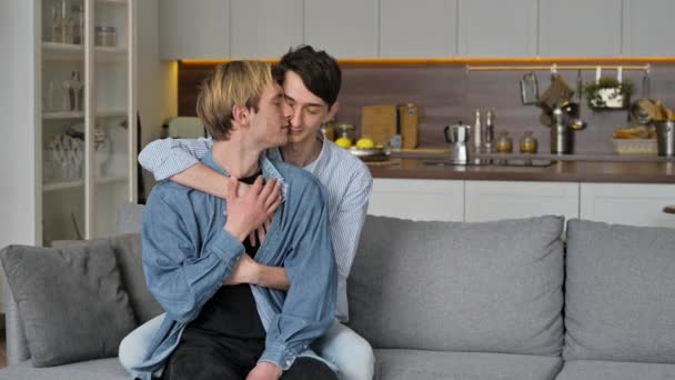Homoseksuaaleja. Rakastava homopari, joka istuu kotona, hellii ja hyväilee toisiaan, rentoutuu yhdessä olohuoneen sohvalla, viettää aikaa yhdessä, samaa sukupuolta oleva pari - Materiaali, video