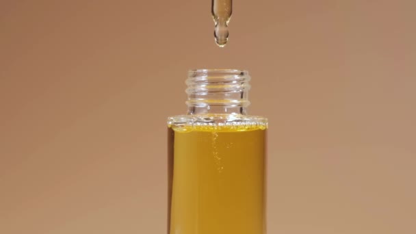 Goteo de aceite de pipeta en botella de vidrio sobre fondo beige. - Imágenes, Vídeo