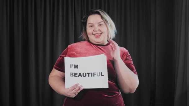 Itsevarma flirttaileva ylipainoinen nainen, jolla on nimikyltti, jossa on merkki IM BEAUTIFUL ja minä rakastan MYSELFiä - Materiaali, video