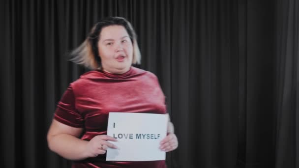 Een zelfverzekerde flirterige dikke vrouw met een naamplaatje met een teken I Love MYSELF - Video