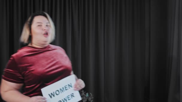 Een zelfverzekerde flirterige dikke vrouw met een naambordje met een bordje VROUWEN KRACHT - Video