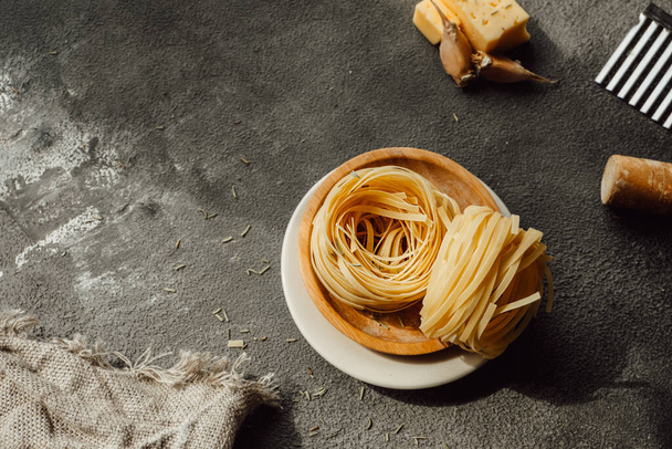 zelfgemaakte Pappardelle rauwe pasta, deegroller, bloem en gekartelde mes in donkere keuken. proces van het maken van handgemaakte pasta van durumtarwe. voedselbloggen. selectieve focus - Foto, afbeelding
