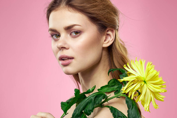 Portret van een vrouw met gele bloemen op een roze achtergrond Make-up op het gezicht - Foto, afbeelding