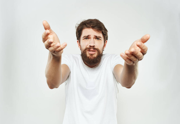 Uomo ammaliato in bianco t-shirt gesticolando con le mani ritagliato vista sfondo luce - Foto, immagini
