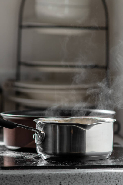 Kookwater met stoom in een pot op een elektrisch fornuis in de keuken. Wazige achtergrond, selectieve focus. - Foto, afbeelding