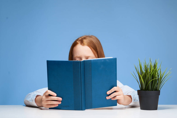 赤い髪の少女は本を手にテーブルに座り - 写真・画像
