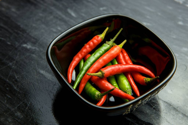 Red and green chilli peppers in black bowl on black background - Photo, Image