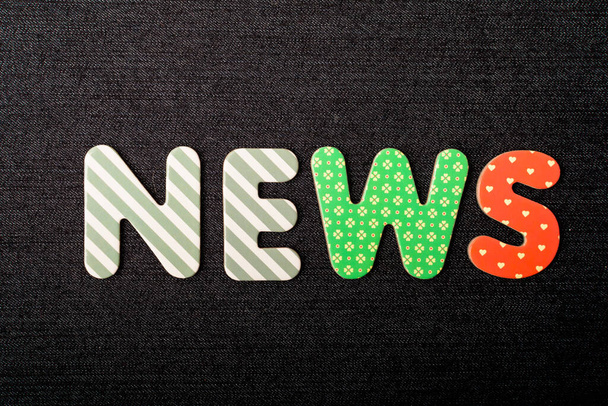 Card with News word made from mixed vivid colored wooden letters on a textured dark black textile material that can be used as a message - Photo, Image