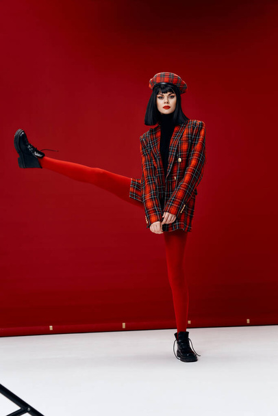 γυναίκα με υψωμένο πόδι μέχρι ποζάρουν σε κόκκινο φόντο κολάν glamor - Φωτογραφία, εικόνα