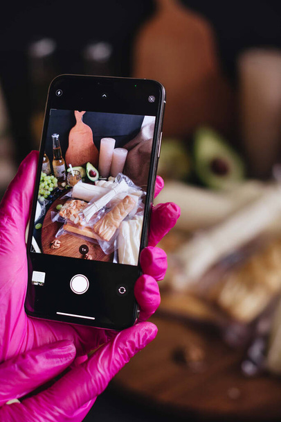 Uma pessoa faz uma foto de produtos de queijo em seu smartphone. Foto de comida em um telefone. - Foto, Imagem