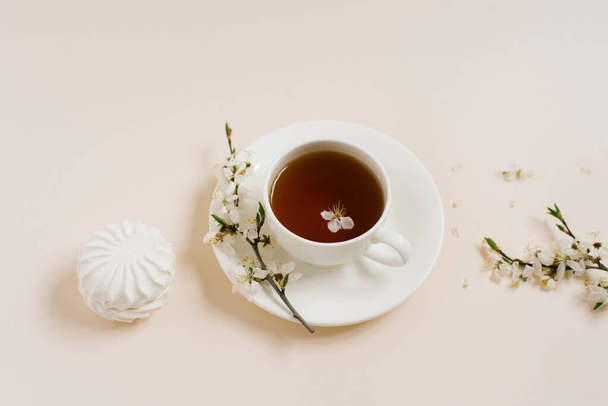 Чашка чаю, що стоїть з яблучними квітами та зефіром на бежевому фоні
 - Фото, зображення