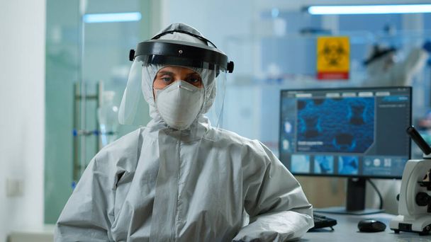 Müder Mikrobiologe in Overall sitzt im Labor und blickt in die Kamera - Foto, Bild