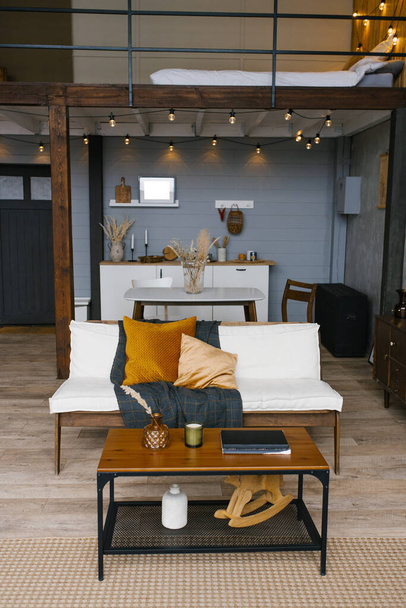 ダイニングルーム、ソファ、コーヒーテーブルの北欧スタイルのインテリアは、灰色とマスタード色のキッチンの背景にあります。 - 写真・画像