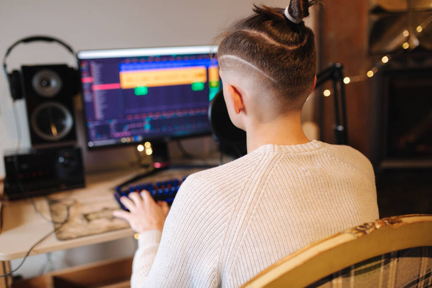Młody, szczęśliwy DJ-man noszący słuchawki i pracujący w domu podczas nagrywania podcastów na pokaz online. Widok z tyłu - Zdjęcie, obraz