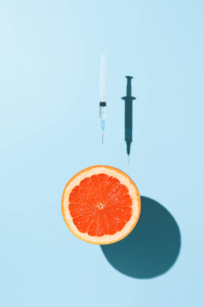 Творча концепція вакцинації Коронавірусу. Половина грейпфрута і шприц з вакциною проти COVID-19, левітуючи над пастельним синім фоном. Мінімалістичний образ зверху. - Фото, зображення