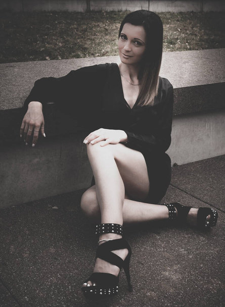 Portrait décoloré de style vintage d'une femme élégante avec vignette assise sur le sol dans un ensemble noir intelligent portant des chaussures à talons hauts - Photo, image