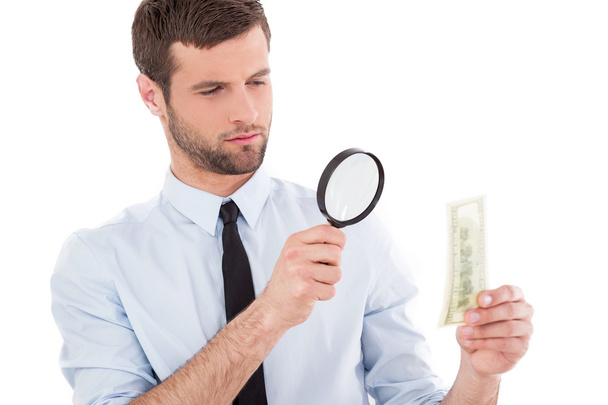 Man looking through a magnifying glass at the paper currency - Photo, Image