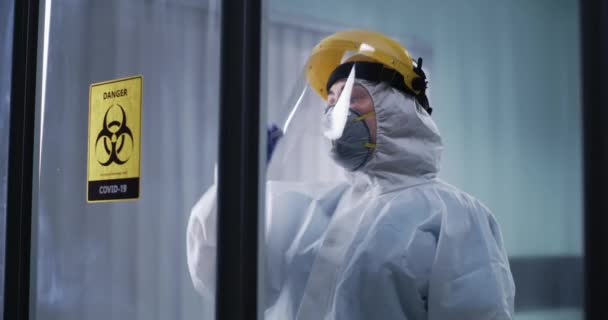 Nainen lääkäri lepää lähellä lasiseinää COVID osastolla - Materiaali, video