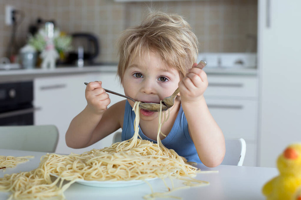 Little blond boy, toddler child, eating spaghetti for lunch and making a mess at home in kitchen - Фото, изображение