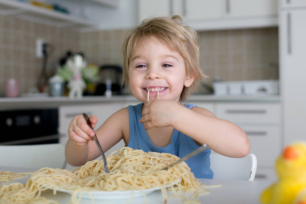 Little blond boy, toddler child, eating spaghetti for lunch and making a mess at home in kitchen - Фото, изображение