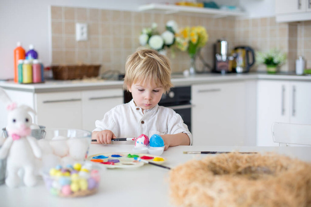 Beautiful blond child, toddler boy, painting easter eggs with mother at home, making easter wreath with rainbow colors - Foto, immagini