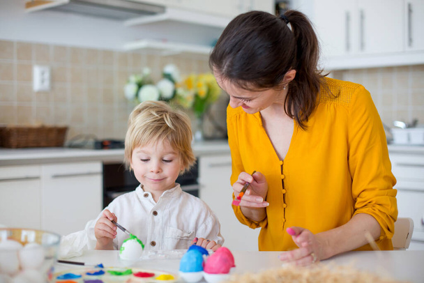 Beautiful blond child, toddler boy, painting easter eggs with mother at home, making easter wreath with rainbow colors - Φωτογραφία, εικόνα