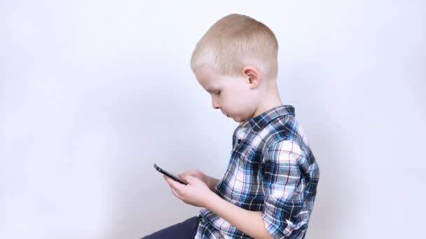 Ребенок играет на смартфоне в видеоигре на белом фоне. Концепция детской зависимости от видеоигр и мобильных телефонов. Сильная привязанность к гаджетам и нежелание заканчивать игры.  - Кадры, видео