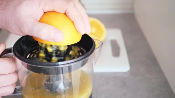 Vista de la mano del hombre mientras se exprime la fruta fresca de naranja en el exprimidor, preparación del desayuno saludable, jugo de vitaminas - Metraje, vídeo