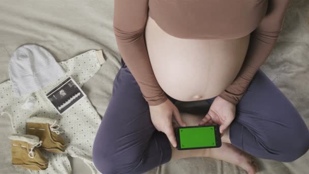 expecting pregnant woman with large belly using smartphone with chromakey on bed - Footage, Video