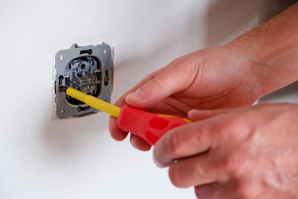 The electrician unscrews the switch with a screwdriver. Close-up on the hands. The routine work of an electrician. Checking contacts. Switch replacement. - Photo, Image