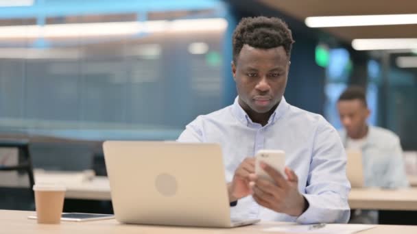 Empresario africano con computadora portátil usando Smartphone en el trabajo - Imágenes, Vídeo