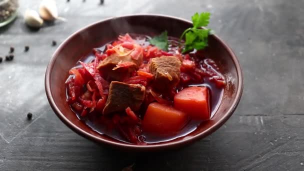 Borsch rojo con verduras y carne en un plato de barro. Vapor de sopa de tomate caliente. Fondo oscuro. Delicioso almuerzo saludable. - Metraje, vídeo