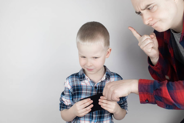 Dad tries to take the child's phone, on which he plays for a long time. The guy does not give up his smartphone and behaves aggressively. Child addiction to mobile phones and video games. - Photo, Image