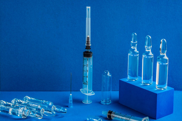 Lékařské jednorázové injekční stříkačky a ampulky s injekcí na modrém pozadí. - Fotografie, Obrázek