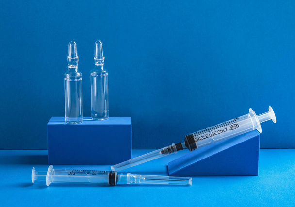 Lékařské jednorázové injekční stříkačky a ampulky s injekcí na modrém pozadí. - Fotografie, Obrázek