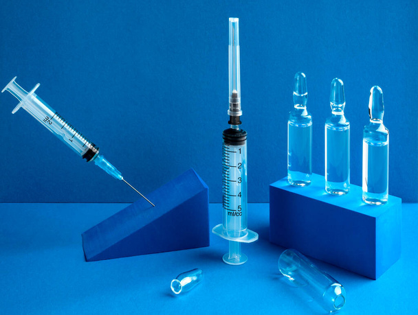 Lékařské jednorázové injekční stříkačky a injekce ve skleněných ampulích. Modré pozadí. - Fotografie, Obrázek