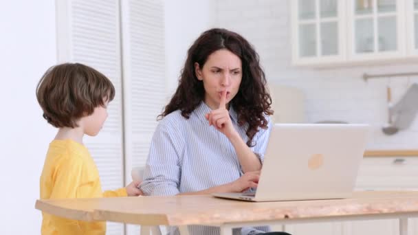 Äiti istuu pöydän ääressä kotona sulkemisen aikana, työskentelee kannettavan tietokoneen, lapsi häiritsee ja tekee melua - Materiaali, video