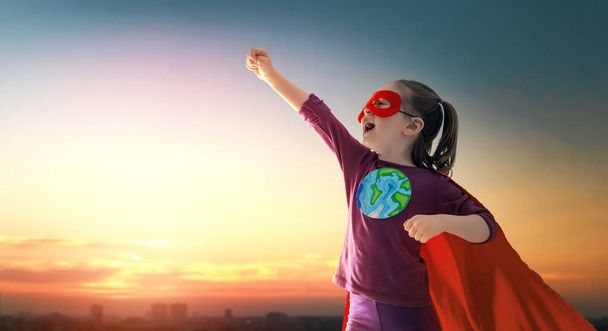 Earth day concept. Child superhero with symbol of ecological worldviews on sunset cityscape background. - Foto, imagen