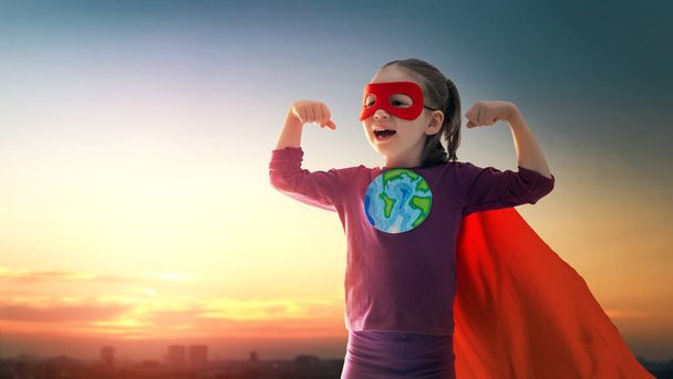 Earth day concept. Child superhero with symbol of ecological worldviews on sunset cityscape background. - Fotoğraf, Görsel
